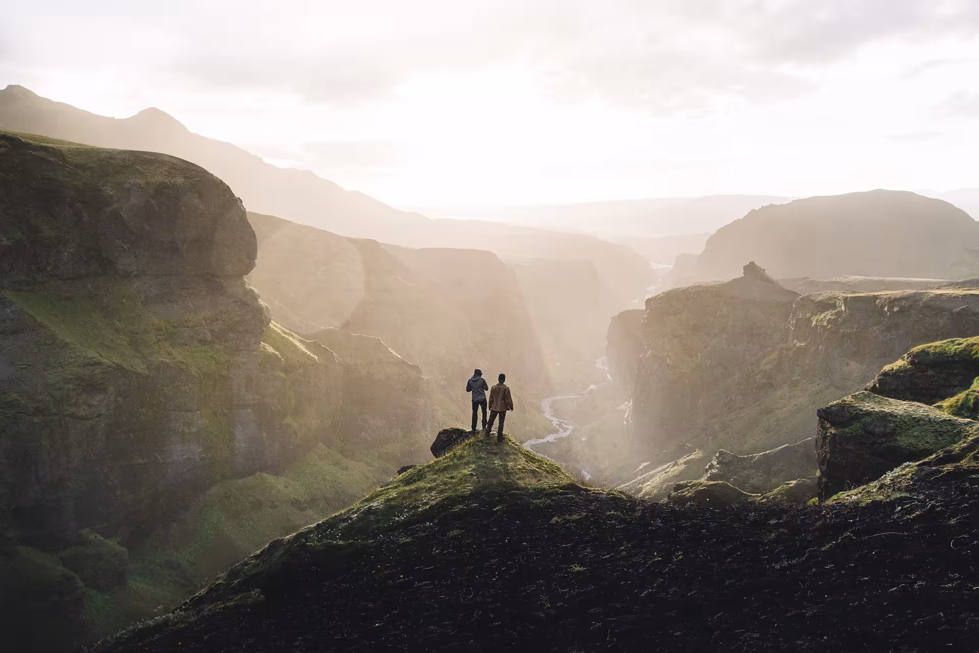 Two hikers standing on a mossy cliff overlooking a dramatic canyon valley in Iceland