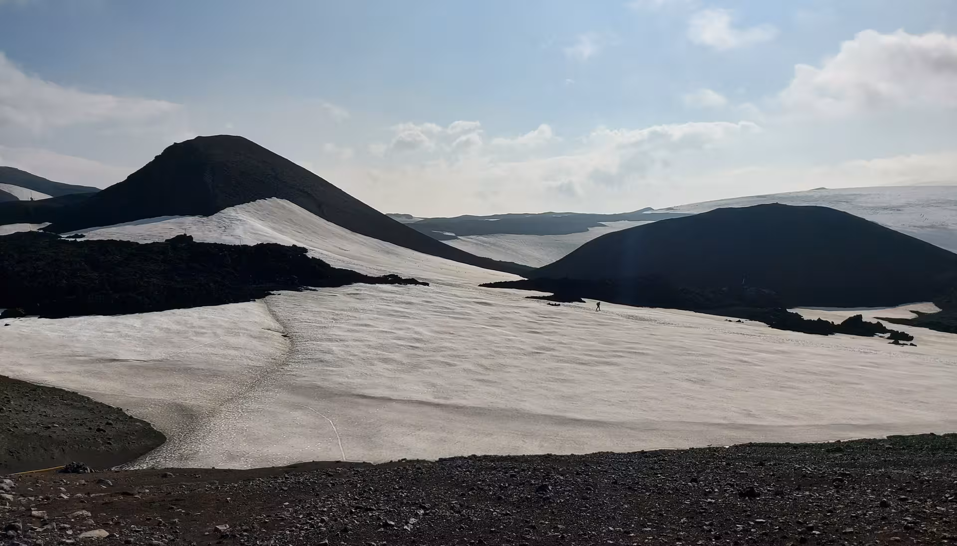 Snow-covered volcanic landscape on Fimmvörðuháls hike Iceland with dark lava hills and lone hiker