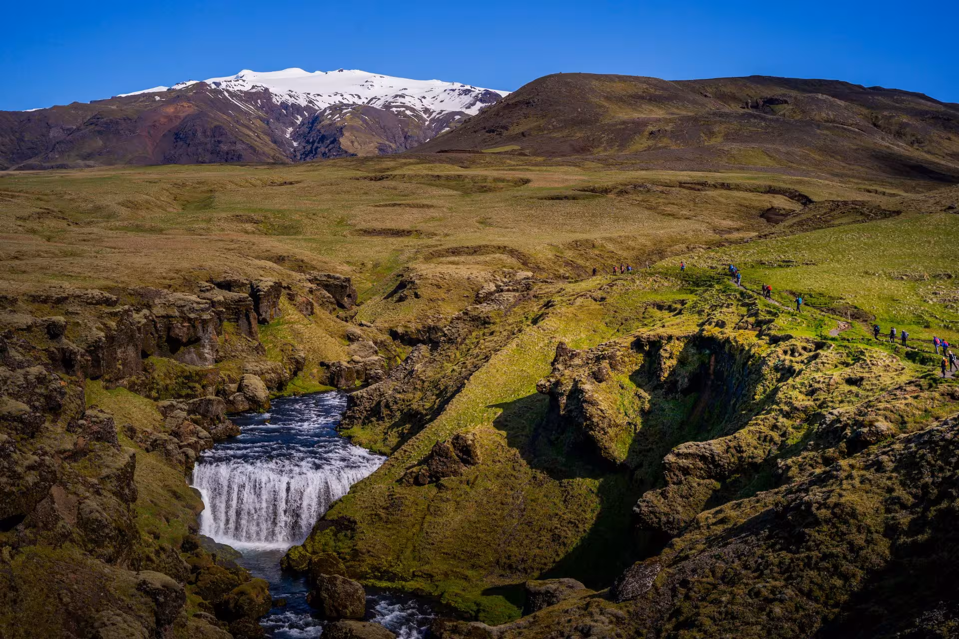 Waterfall cascading through mossy canyon on Fimmvörðuháls hike with snow-capped Eyjafjallajökull volcano in background