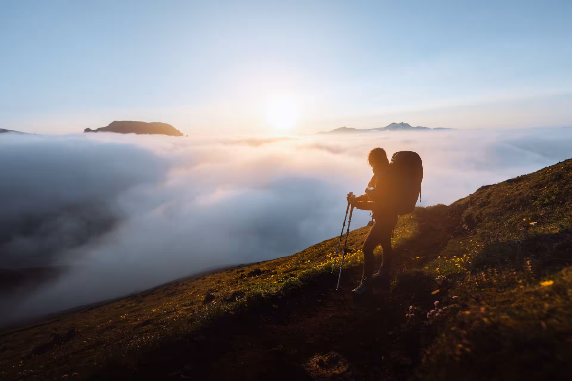 Hiker with trekking poles and backpack on Fimmvorduhals trail above clouds at sunrise in Iceland