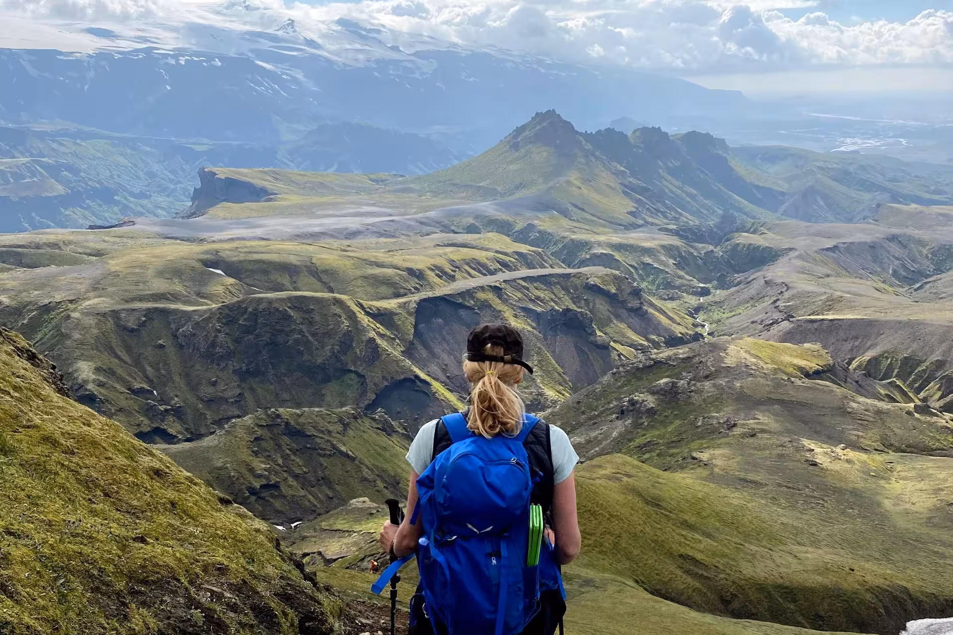 Hiker with blue backpack and trekking poles overlooking green volcanic mountains on Fimmvorduhals trail, Iceland