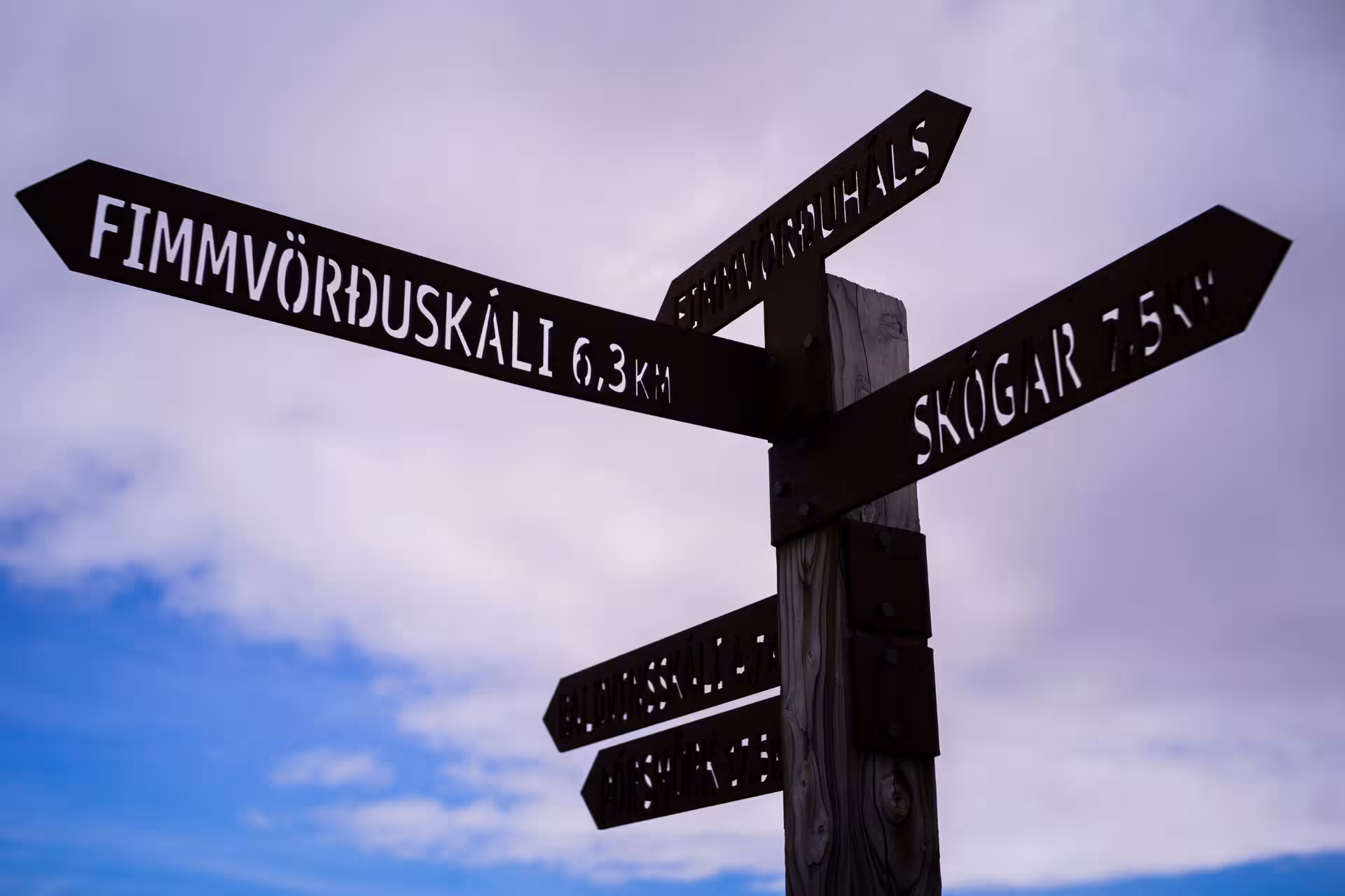 Wooden trail signpost showing Fimmvörðuskáli 6.3km and Skógar 7.5km on Fimmvörðuháls hiking trail, Iceland