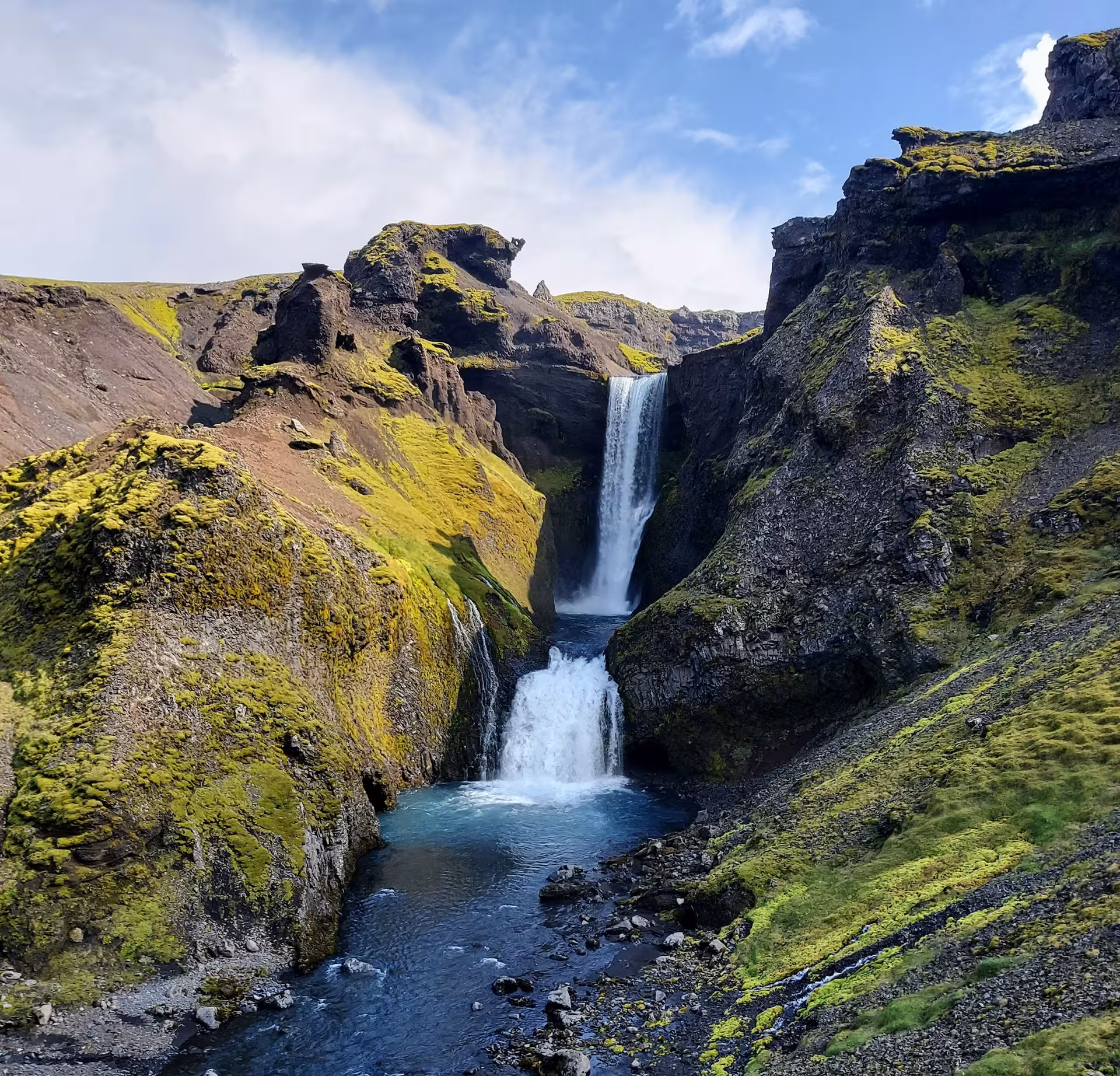 Cascading waterfall flowing through mossy volcanic canyon on Fimmvorduhals hiking trail, Iceland
