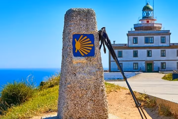 Scenic view of Finisterre lighthouse with walking sticks and Camino de Santiago marker on a sunny day.