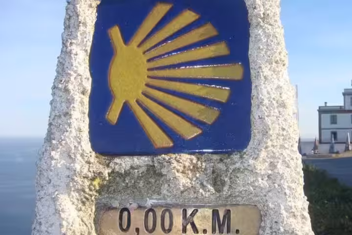 The iconic 0.00 km marker at Finisterre Lighthouse, symbolizing the end of the Camino de Santiago pilgrimage.