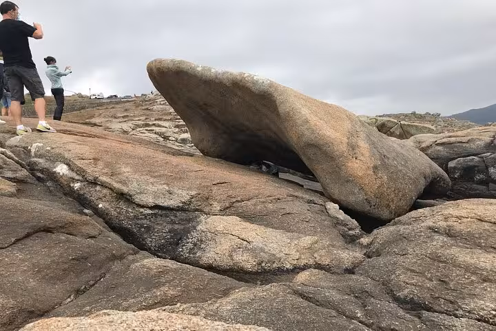 Tourists exploring the unique rock formations at Costa da Morte during the Finisterre and Muxia excursion.