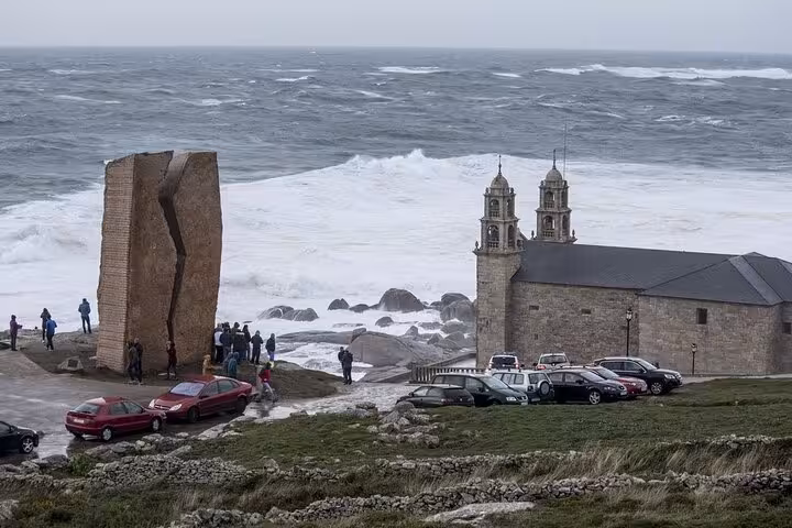 Visitors explore the rugged coastline by Muxia's church with crashing waves, a must-see on Costa da Morte excursions.