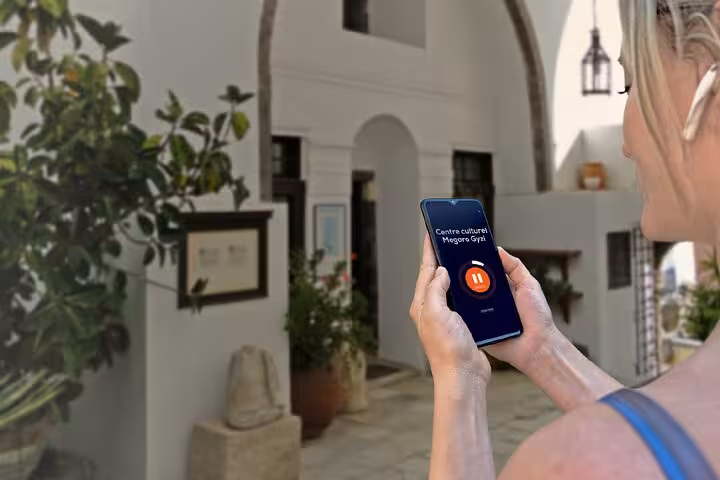 Woman holding smartphone with audio guide app at Megaro Gyzi cultural centre in Fira, Santorini