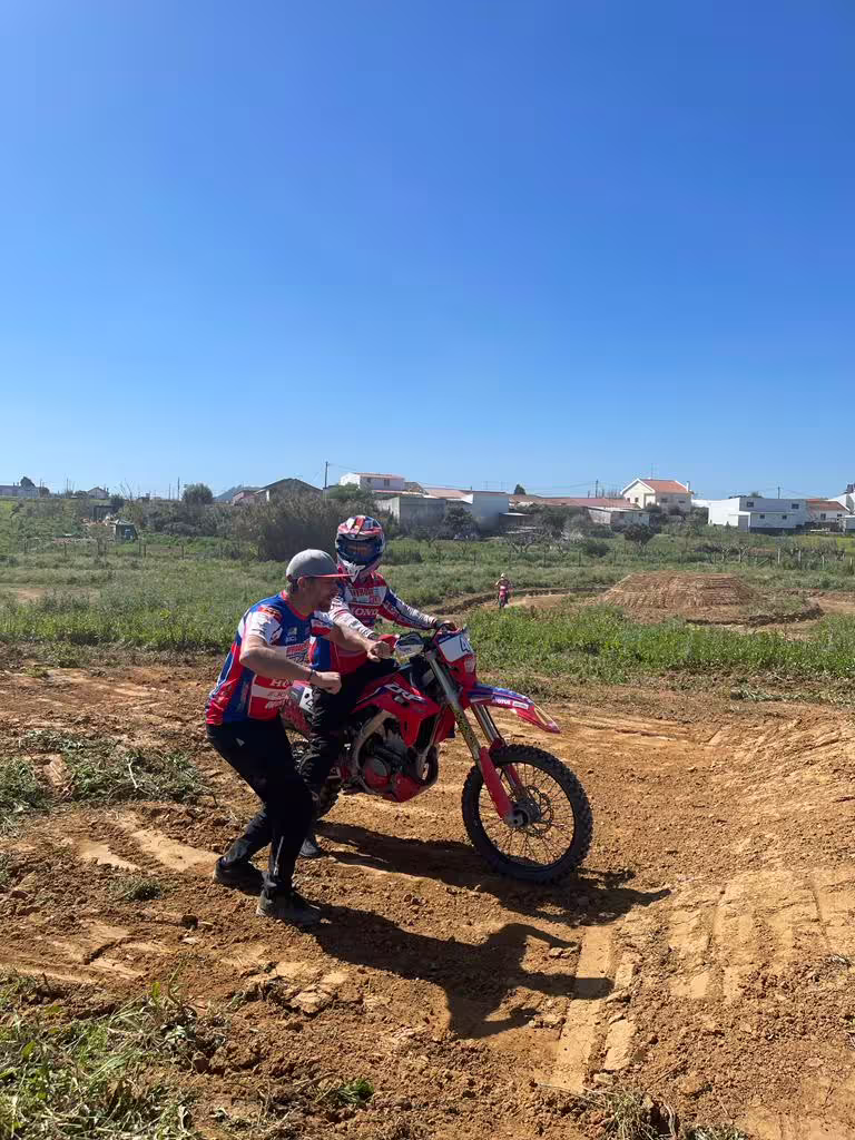 Instructor assisting a rider on a red dirt bike during First Ride Enduro Experience in Carregado, Lisbon under clear blue skies.