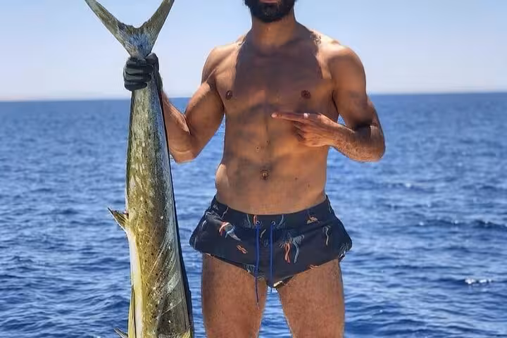 Fisherman holding a big mahi-mahi on a Hurghada deep sea fishing tour in the Red Sea, sunny offshore day
