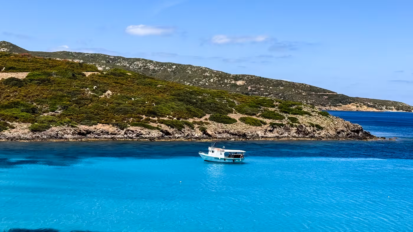A fishing boat anchored in the turquoise waters of Asinara Park, surrounded by lush green hills and clear skies.