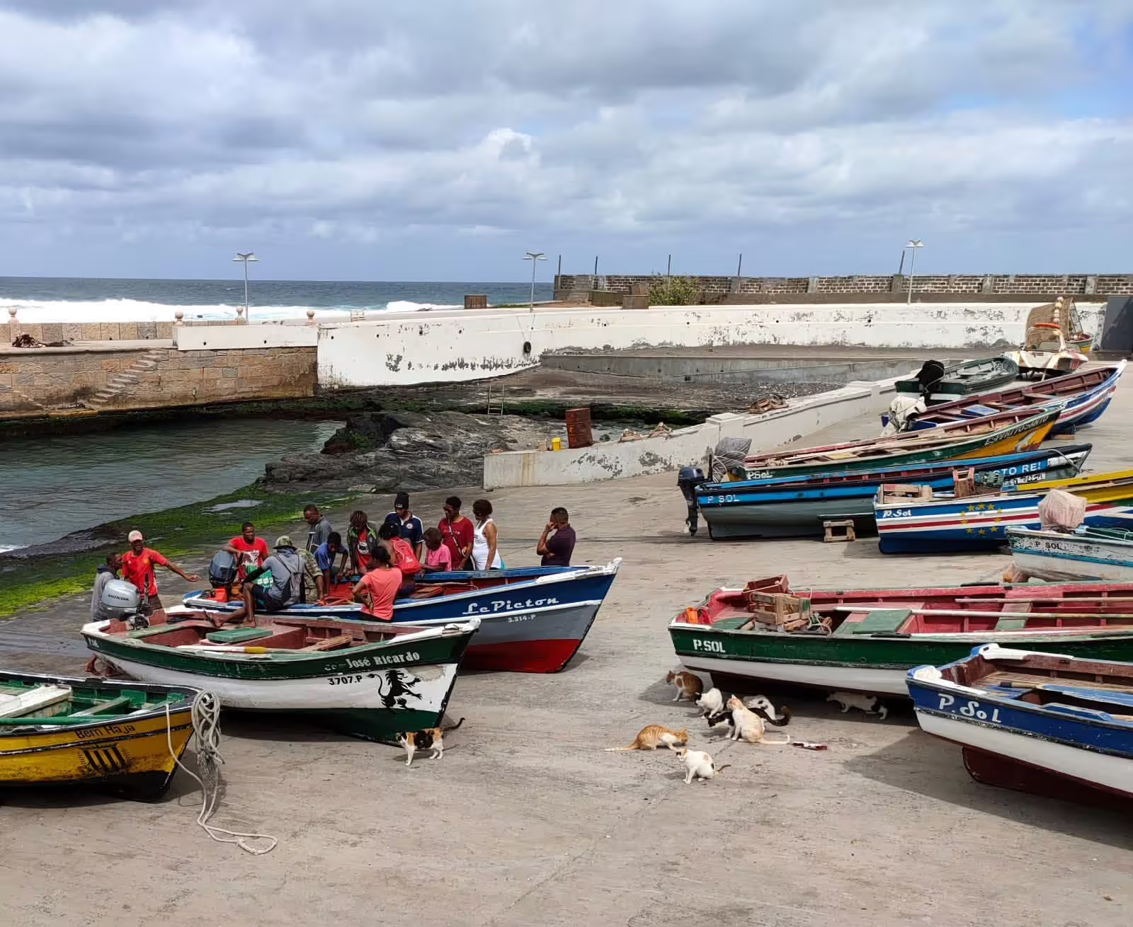 Colorful fishing boats docked with locals gathering at the harbor in São Vicente, gateway to the Santo Antão Valley trek.