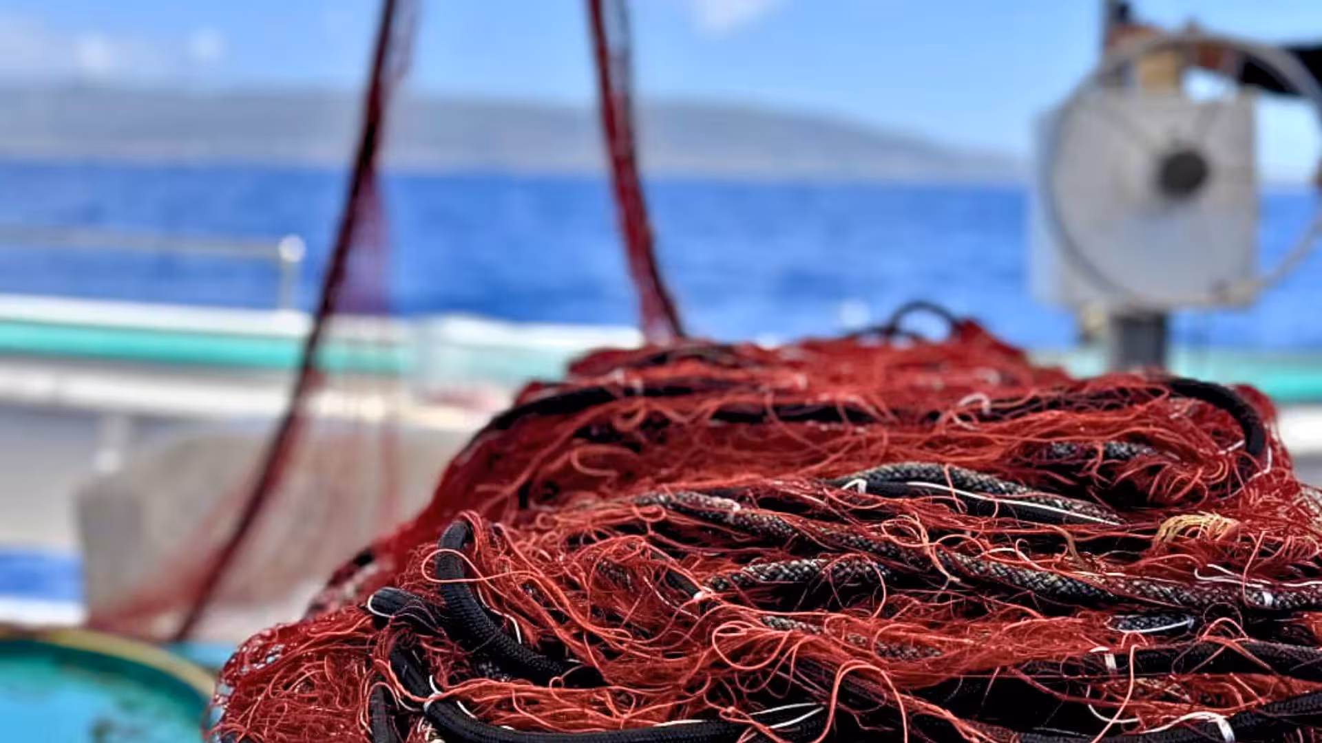 Close-up of fishing nets on a boat in Asinara Park, with vibrant blue sea and distant hills in the background.