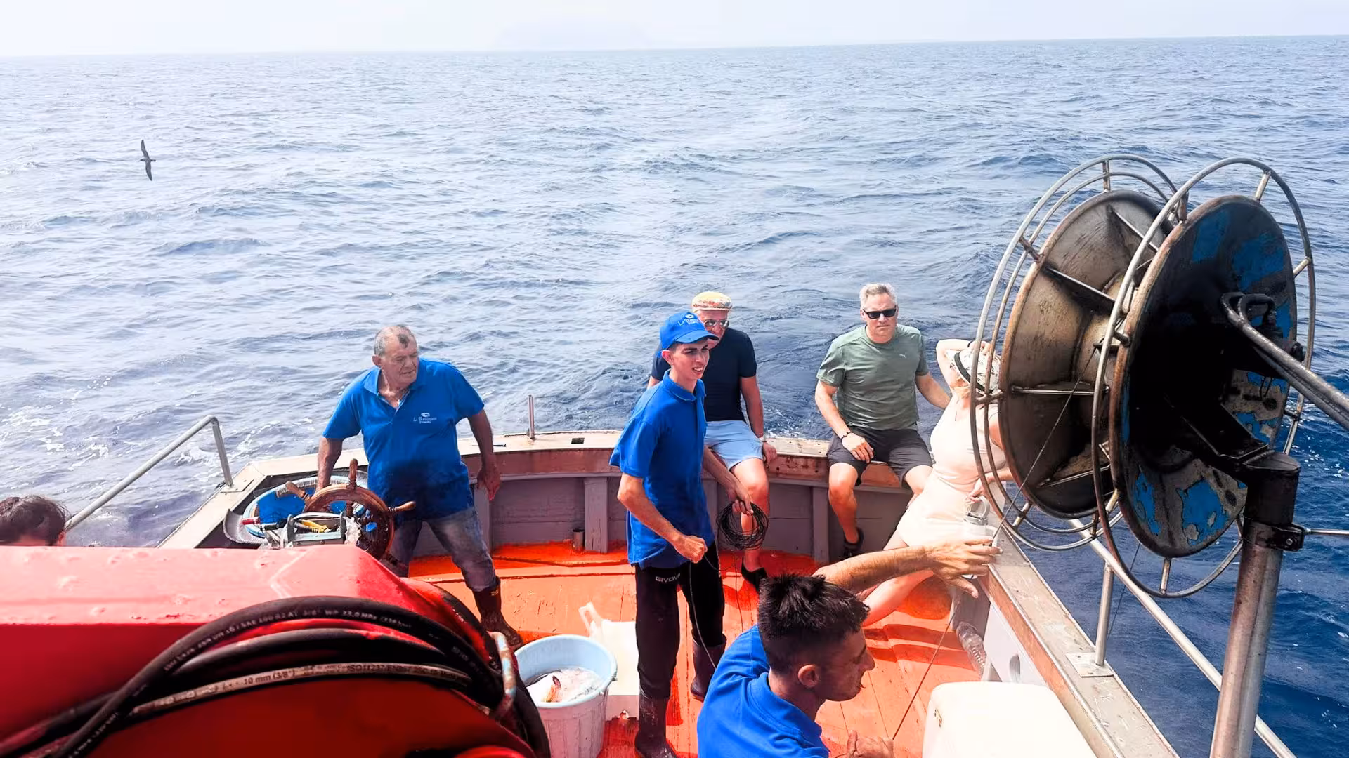 Tourists and crew enjoying a fishing trip on a boat in the Egadi Islands, with scenic ocean views.