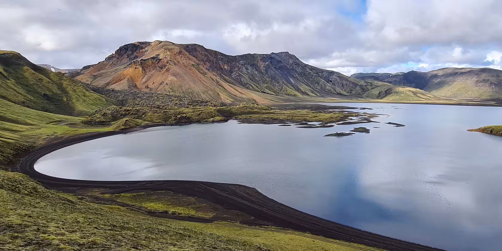 Glacial lake with black volcanic shores surrounded by colorful mountains in Fjallabak Nature Reserve, Iceland