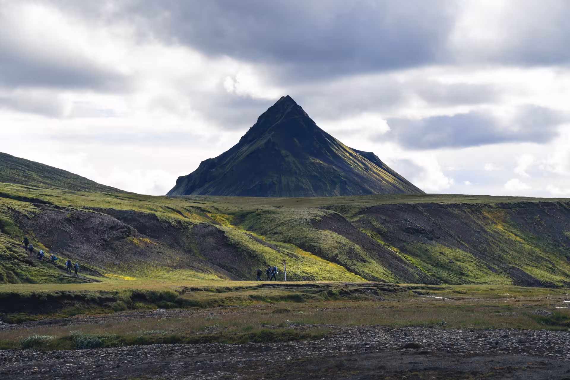 Hikers trekking through green Fjallabak Nature Reserve with dramatic pyramidal volcanic mountain peak
