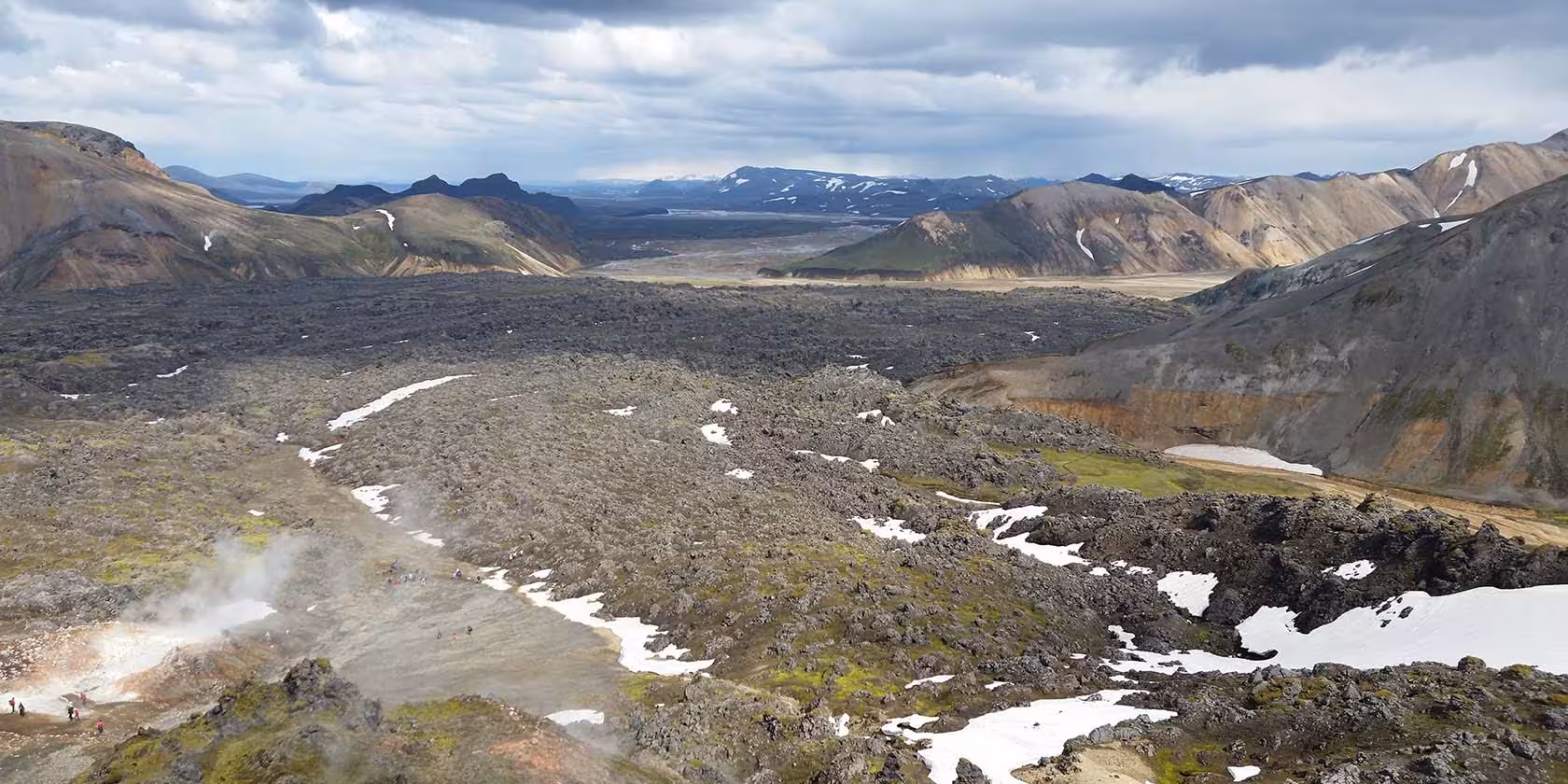 Aerial view of Landmannalaugar lava field with geothermal steam, snow patches, and colorful rhyolite mountains in Fjallabak Iceland