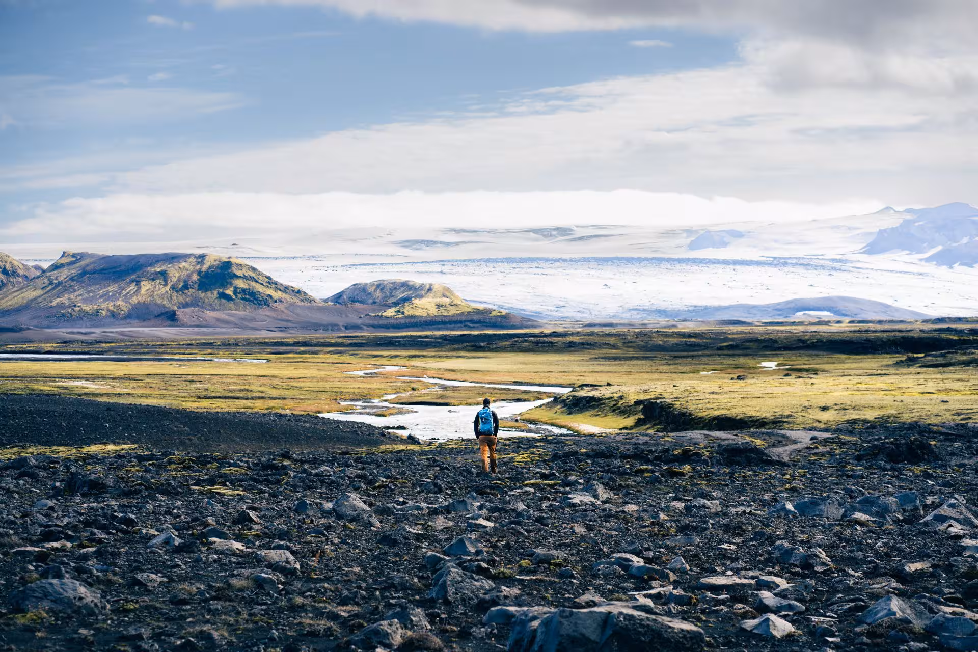 Hiker with blue backpack overlooking Fjallabak volcanic landscape with glacier and winding river beyond