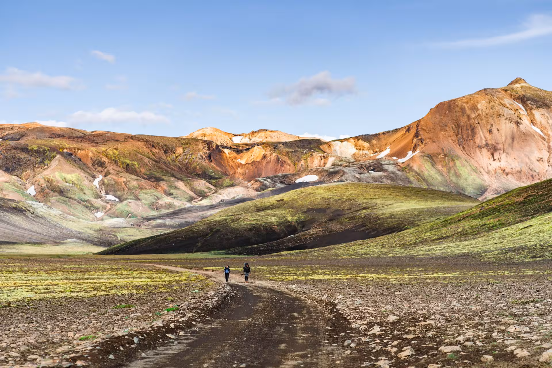 Two hikers walking a dirt trail through Fjallabak Nature Reserve with colorful rhyolite mountains