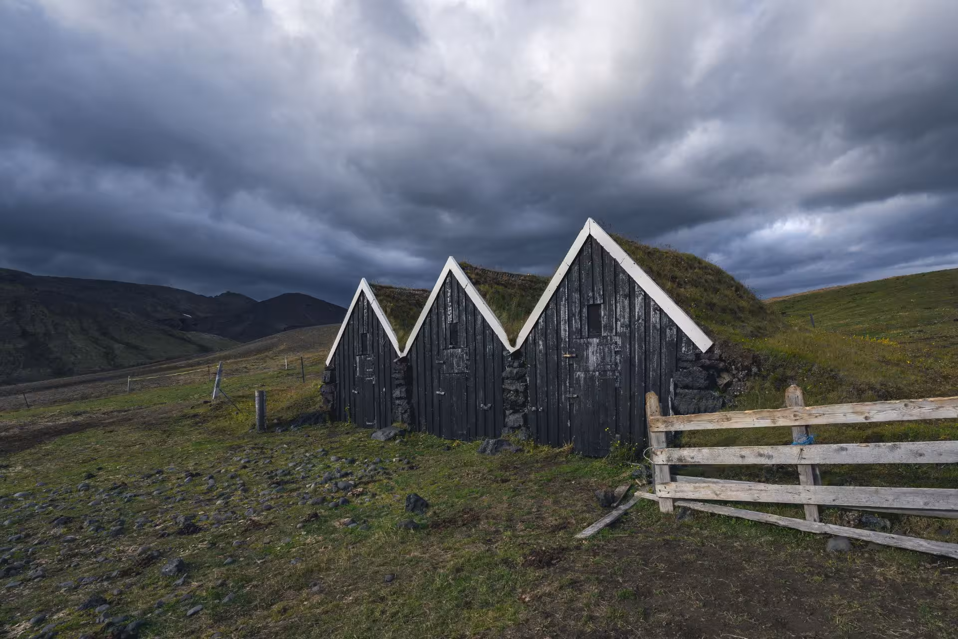 Traditional dark wooden turf-roofed sheds in Fjallabak Nature Reserve under dramatic stormy sky