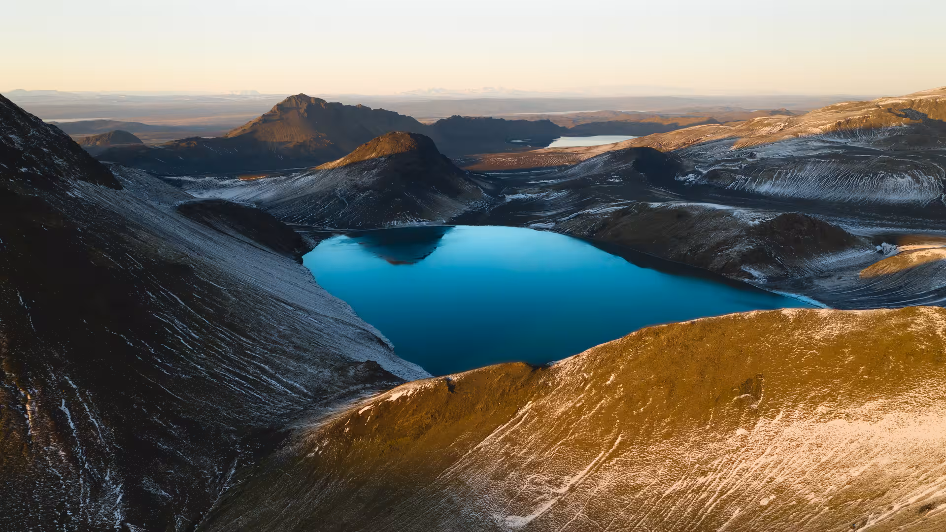 Vivid turquoise crater lake nestled among snow-dusted volcanic mountains in Fjallabak, Iceland