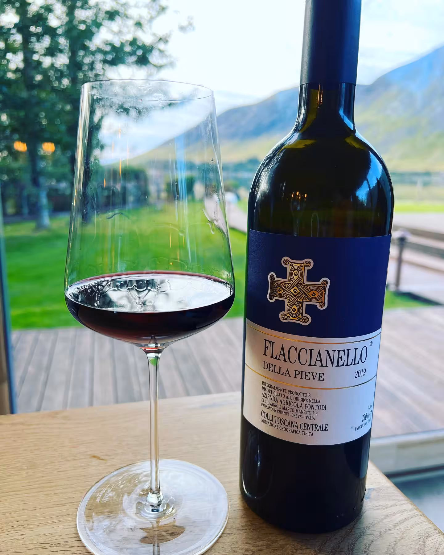 Flaccianello Della Pieve 2019 Italian red wine glass and bottle with stunning lake and mountain backdrop for food pairing tour.