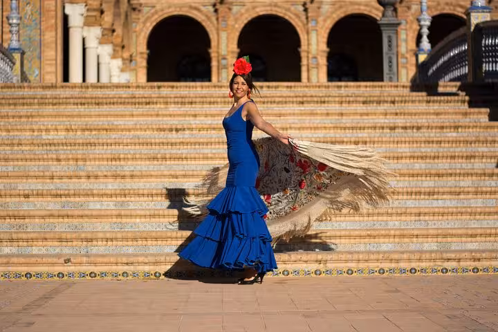 Flamenco dancer in vibrant blue dress twirling with a fan at Plaza de España, Seville, highlights Andalusia's cultural charm.
