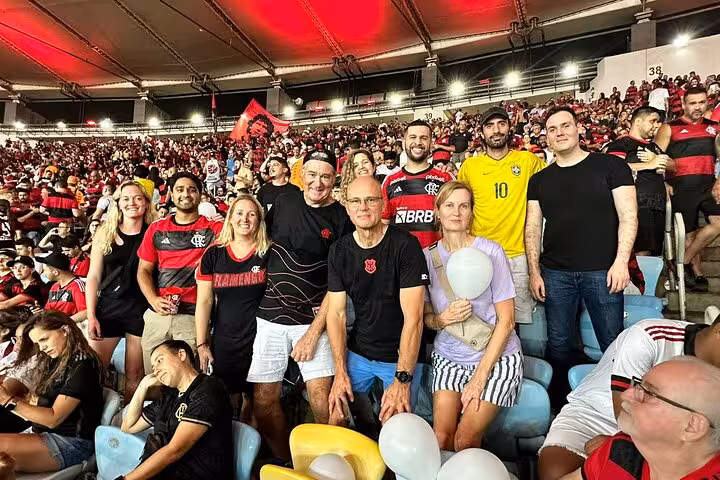 Tour group at Maracanã Stadium cheering Flamengo match, wearing red-black jerseys amid packed Rio crowd
