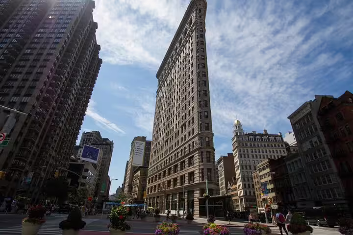 Flatiron Building in New York City at a busy street intersection with blue sky