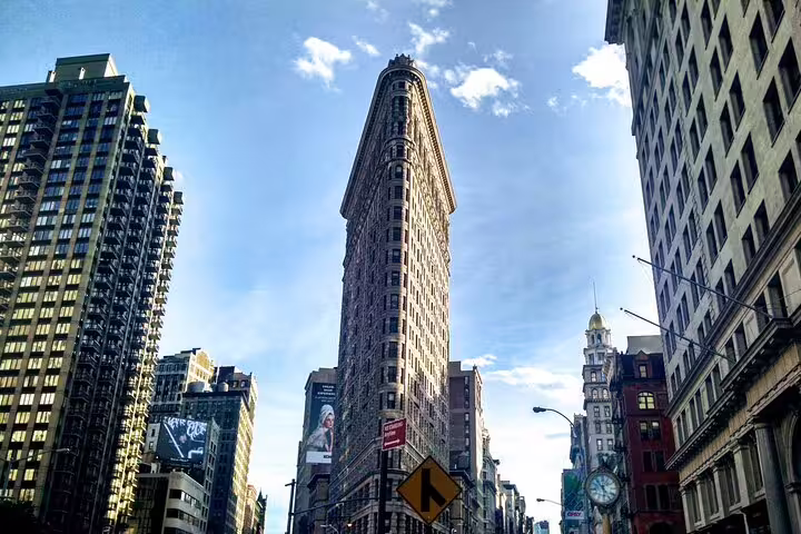 Iconic Flatiron Building triangular facade rising above Manhattan streets with surrounding NYC skyscrapers
