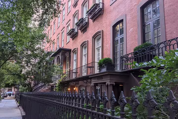 Historic red brick brownstone townhouses with ornate iron fencing on a tree-lined street in Flatiron NYC