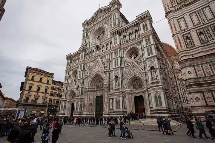 Crowds of tourists in front of Florence Cathedral's ornate white and green marble facade