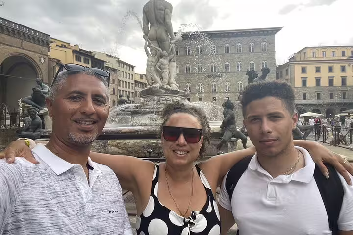 Three tourists smiling in front of Neptune Fountain at Piazza della Signoria, Florence