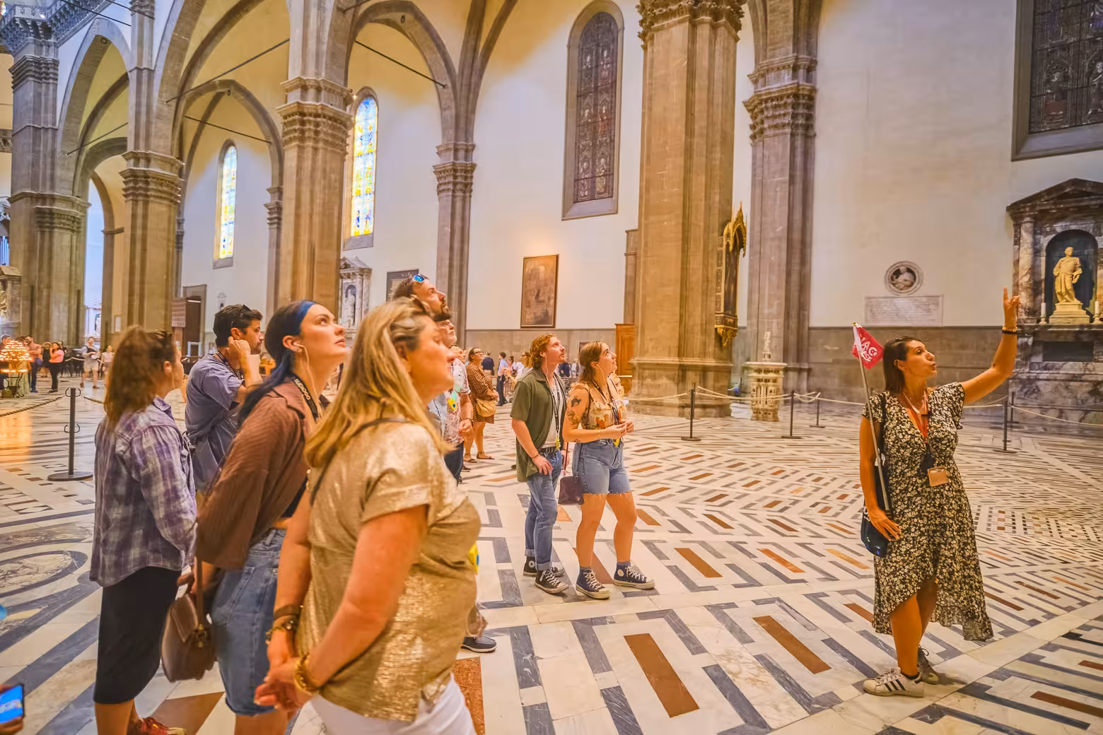Guide points out features in Florence's Duomo as tourists admire the historic cathedral's interior.