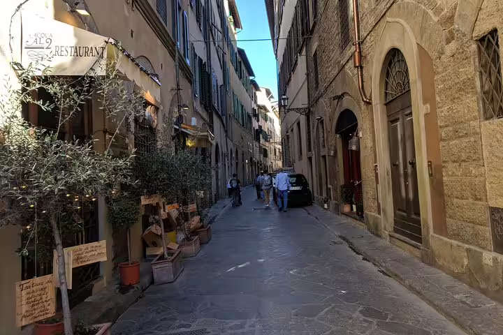 Narrow medieval street in Florence with historic stone buildings and pedestrians walking