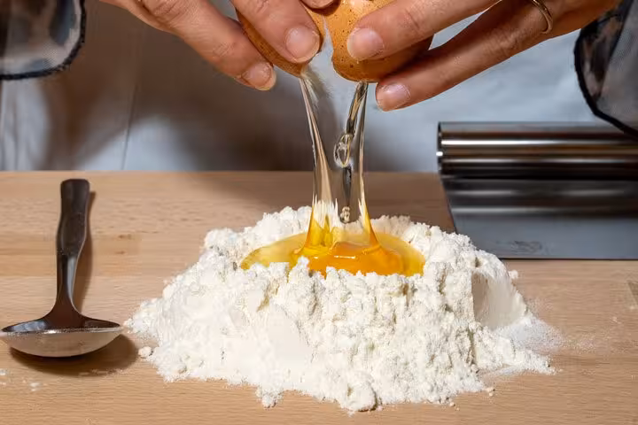 Hands cracking an egg into a flour mound for pasta making during a Florence cooking class with unlimited wine.