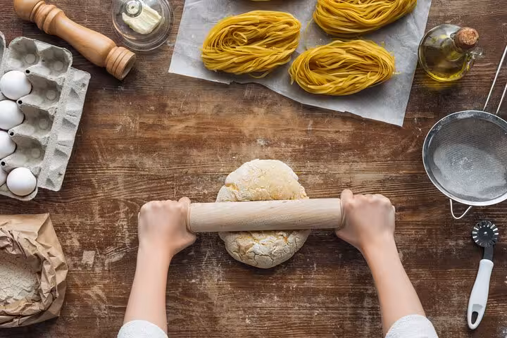 Rolling dough on a wooden table surrounded by fresh pasta ingredients at a Florence cooking class experience.