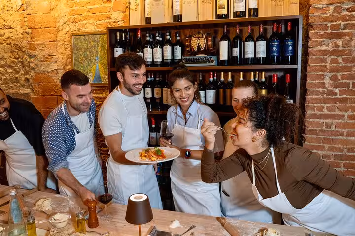 Group enjoys tasting pasta creation during lively Florence cooking class with unlimited wine.