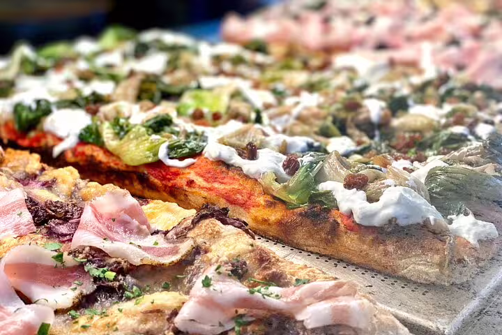 Close-up of authentic Florentine pizza al taglio topped with fresh vegetables and prosciutto on a walking food tour