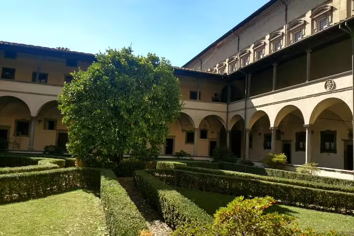 Sunlit Renaissance courtyard with arched colonnades and manicured hedges in Florence