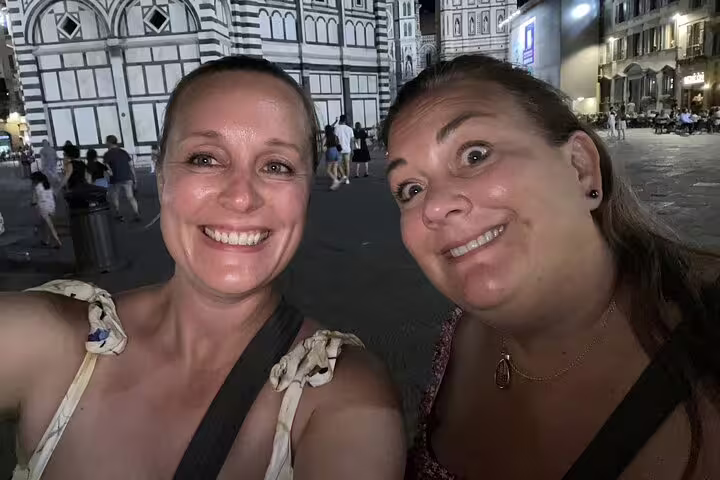 Two women smiling at night in Florence's Piazza del Duomo cathedral square