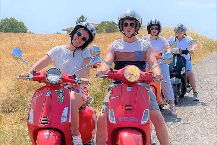 Group of friends riding red Vespas through the sunlit Tuscany countryside, part of a Florence day tour with wine tasting.