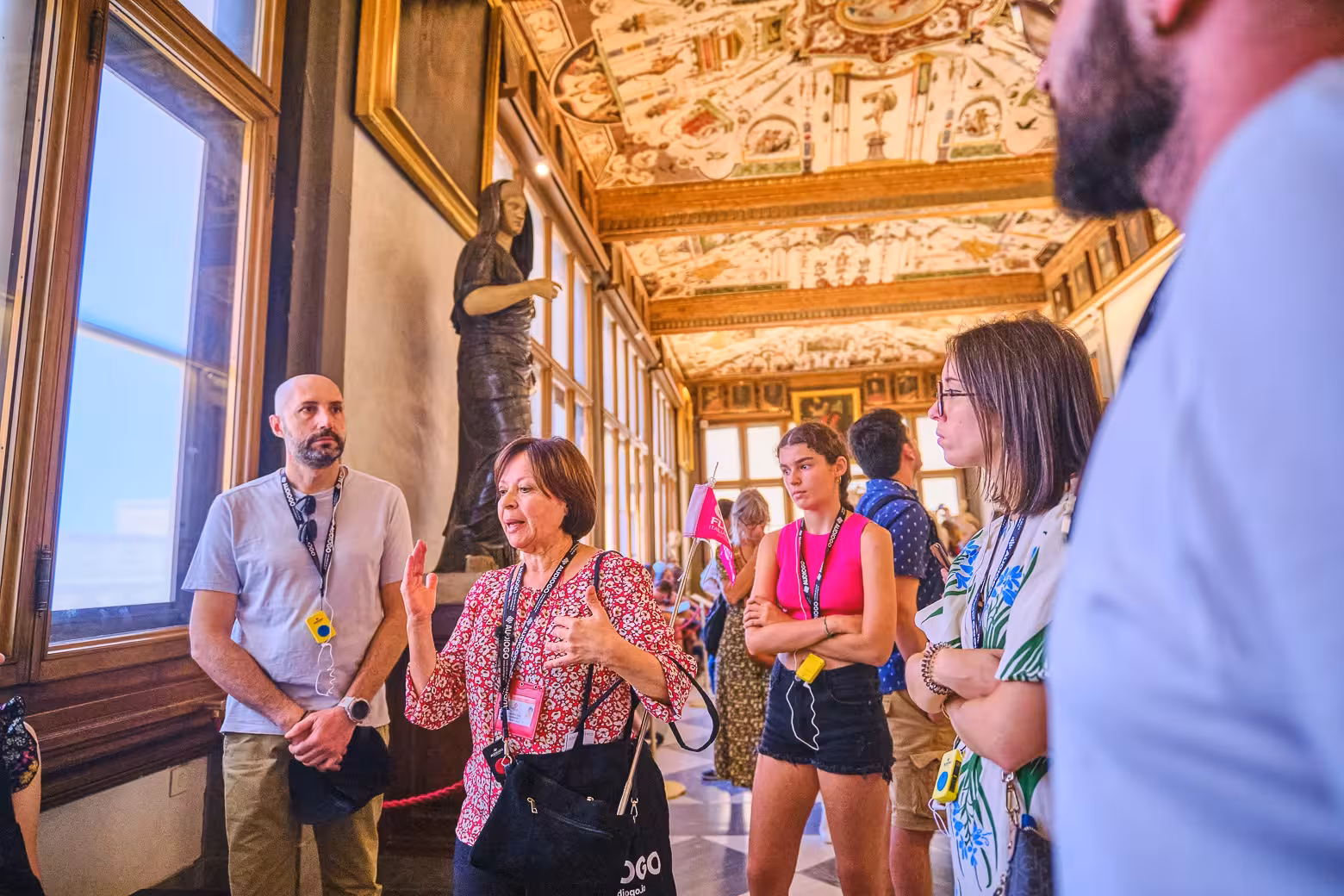 Group of tourists on a guided tour at Florence's Uffizi Gallery, admiring artwork and architecture.