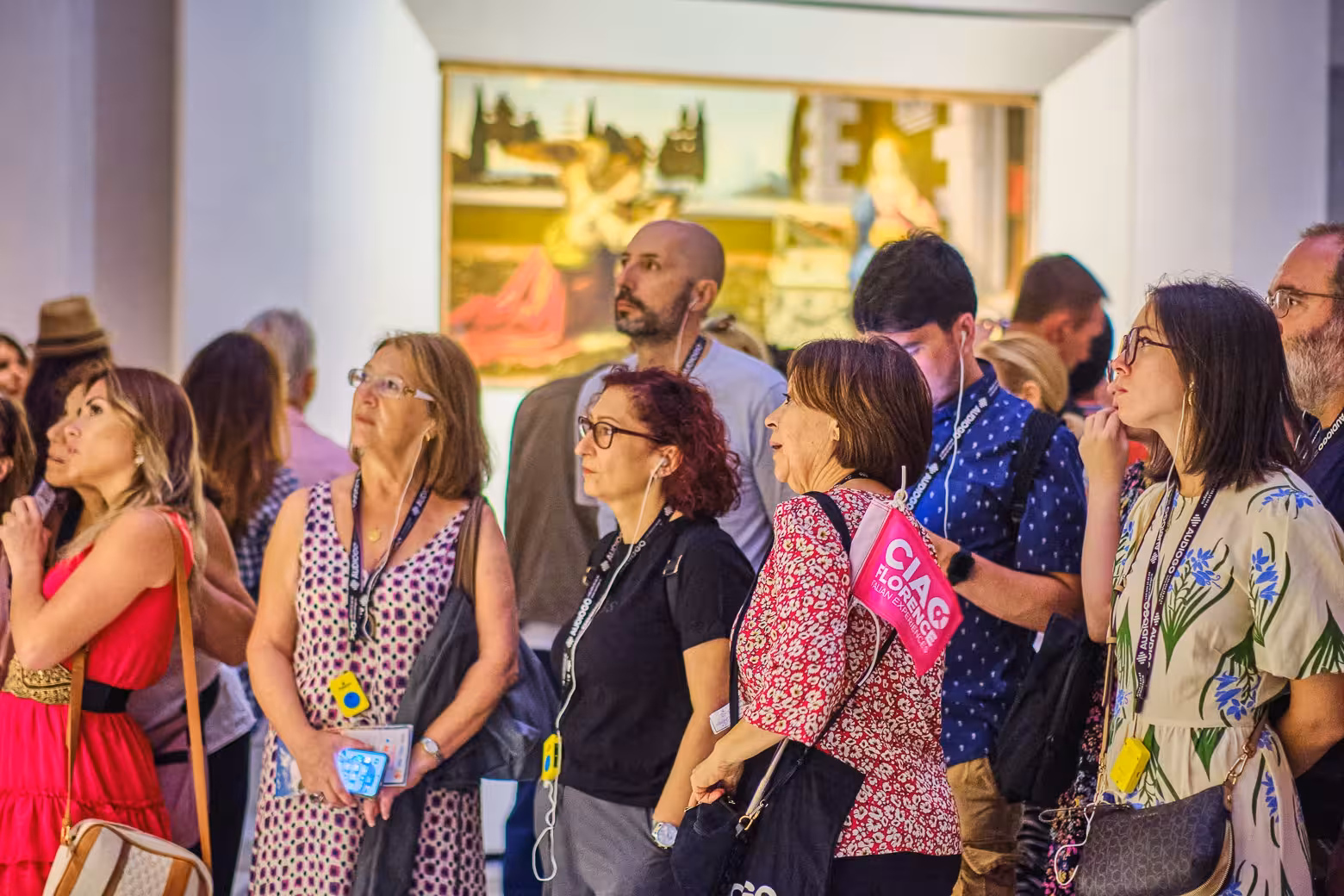 Visitors engaged in a guided tour at Florence's Uffizi Gallery, observing famous artworks with audio guides.
