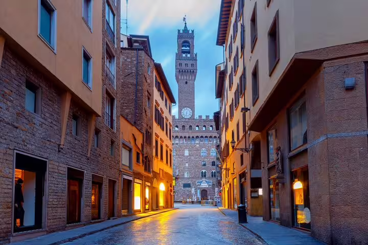 Narrow cobblestone street leading to Palazzo Vecchio tower in Florence at dusk