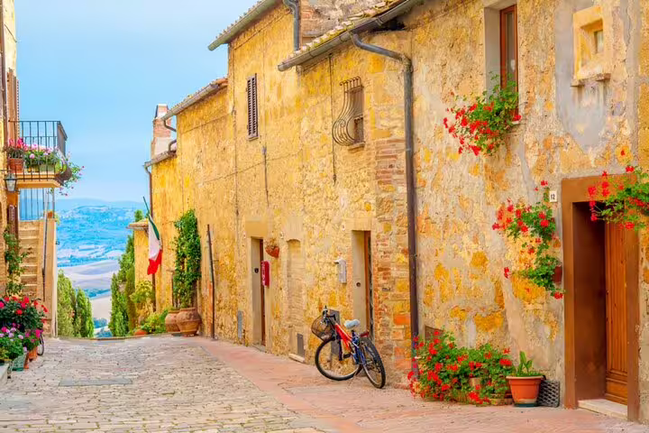 Cobblestone street lined with golden stone buildings and red flowers in a Tuscan hilltop village, Italy