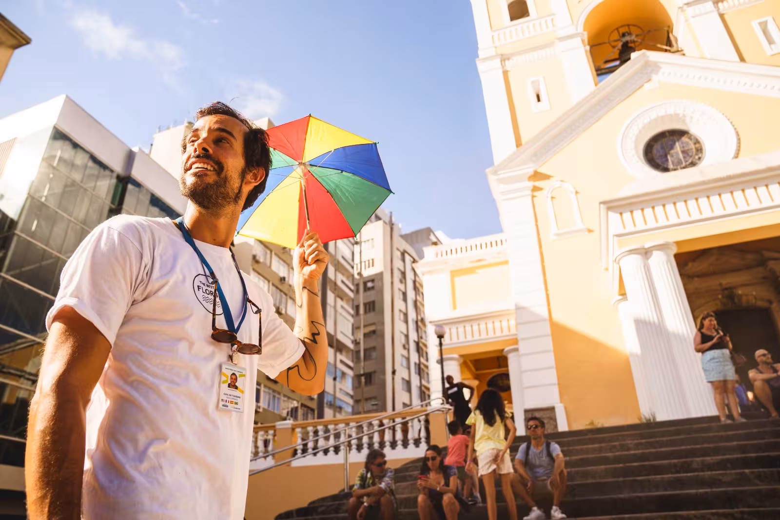 Tour guide with colorful umbrella leads group near historic yellow building in Florianopolis walking tour.