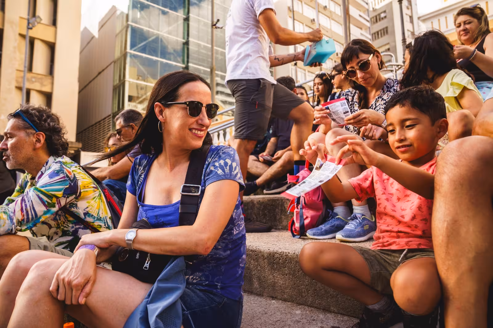 Visitors sitting on steps, enjoying a lively Florianopolis walking tour with tickets in hand.