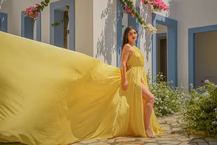 Woman in a flowing yellow dress poses elegantly in a sunlit courtyard adorned with flowers in Hersonissos.