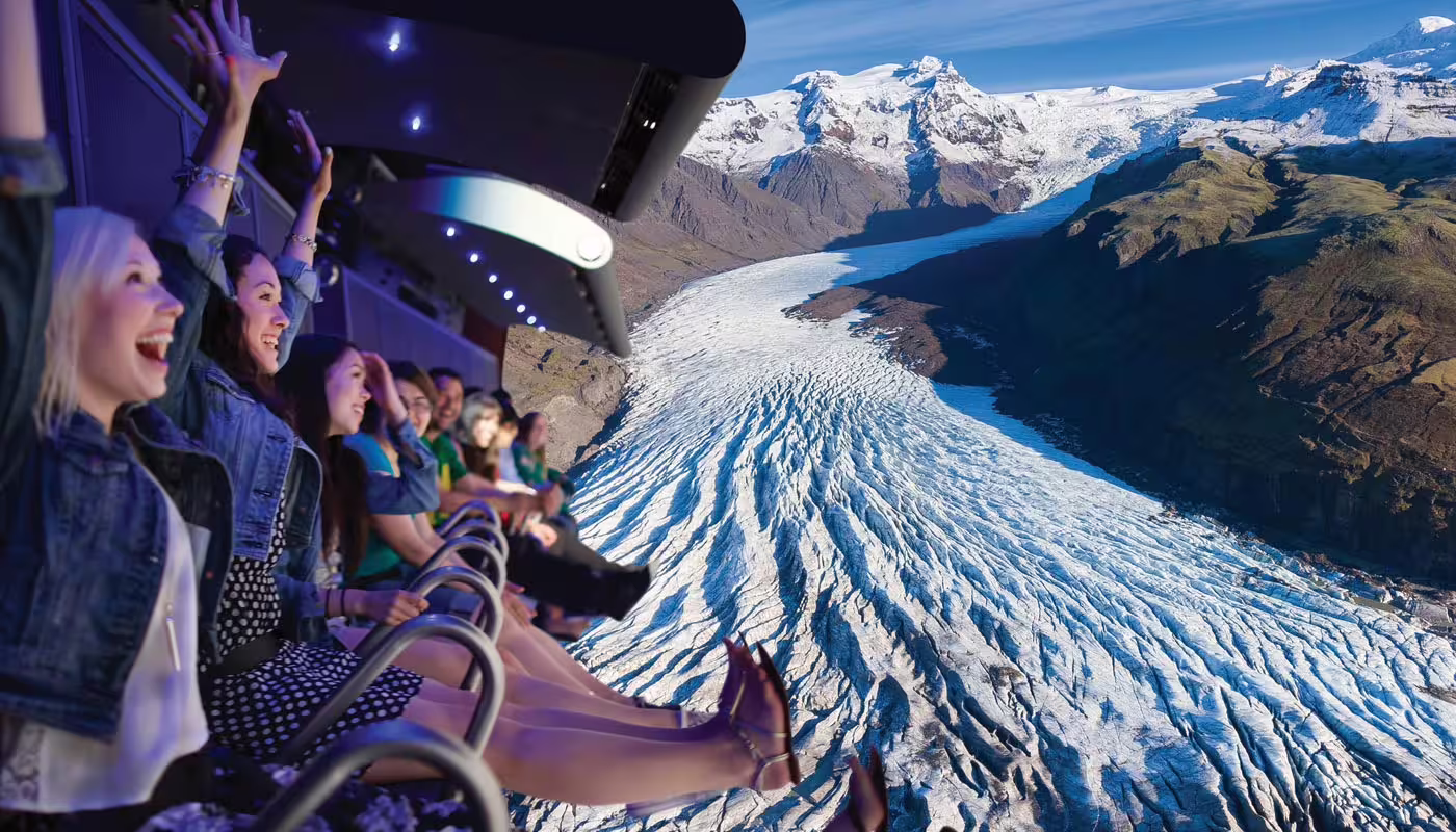 Excited visitors on FlyOver Iceland simulator seats soaring over a massive glacier and snow-capped mountains